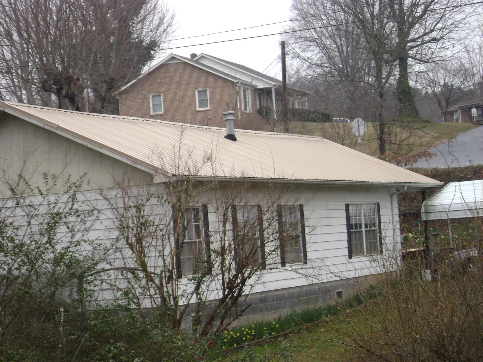Tan metal roof on a white sided house set into a hillside — Commercial Roofing by Roofing Brothers in Spring Grove